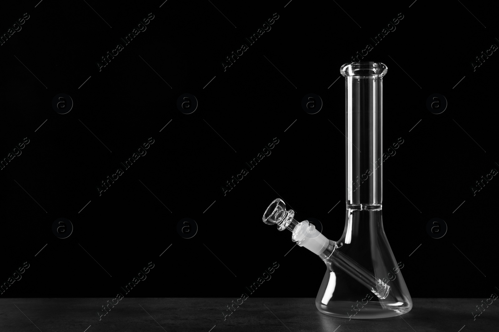 Photo of Glass bong on grey table against black background, space for text. Smoking device