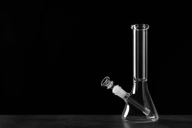 Photo of Glass bong on grey table against black background, space for text. Smoking device