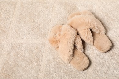 Photo of Fluffy beige slippers on soft carpet, space for text