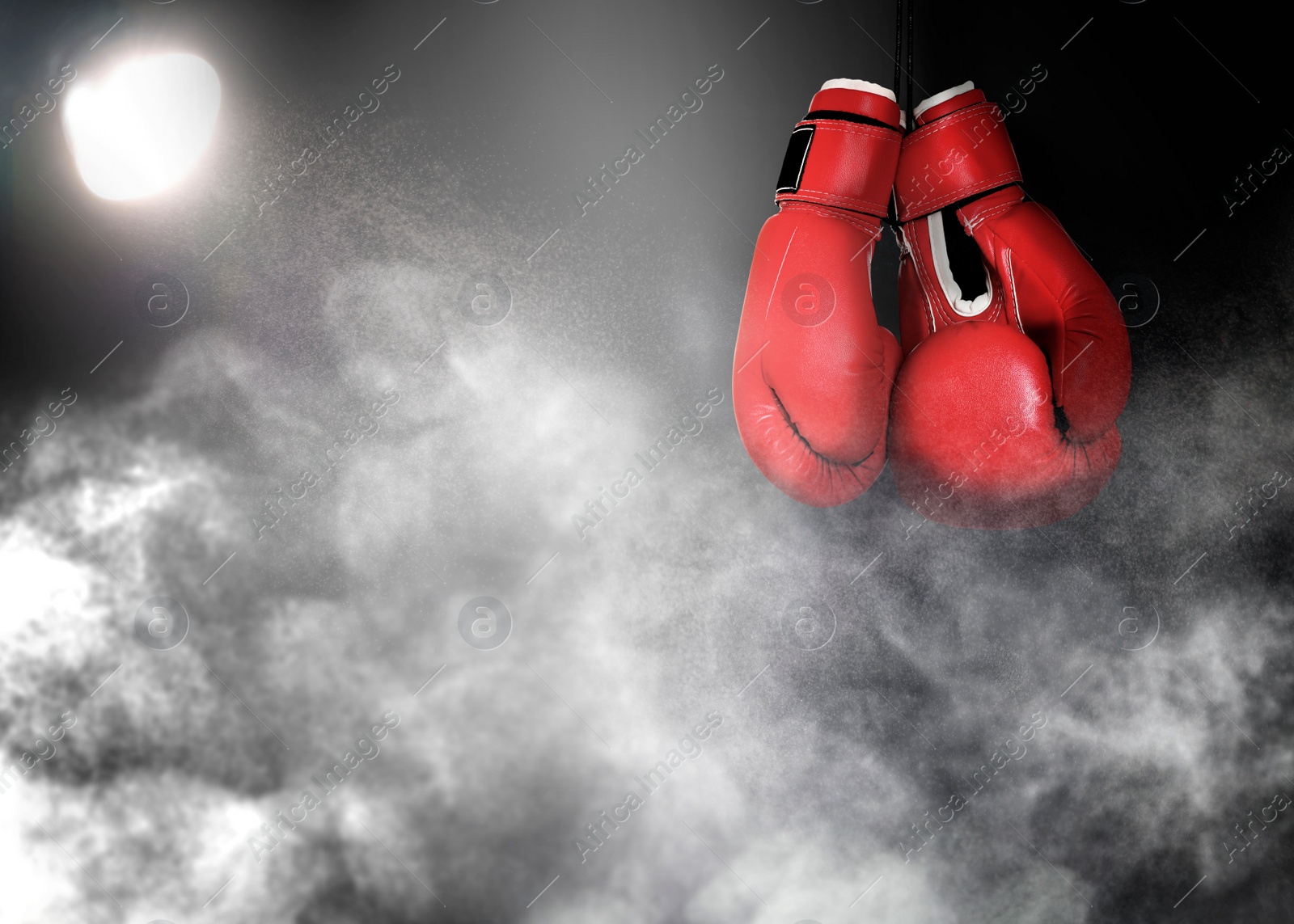 Image of Pair of boxing gloves and white smoke illuminated by spotlight on dark background