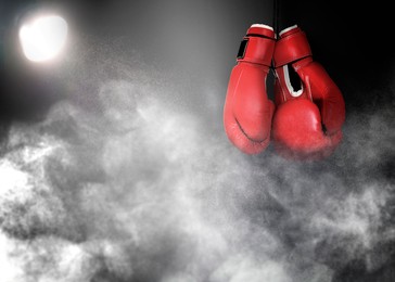 Image of Pair of boxing gloves and white smoke illuminated by spotlight on dark background