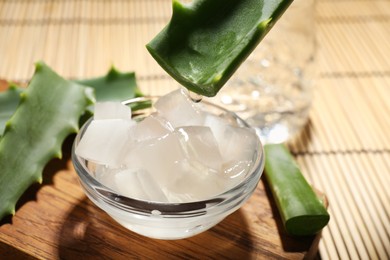 Pouring aloe vera gel from leaf into bowl at bamboo mat, closeup