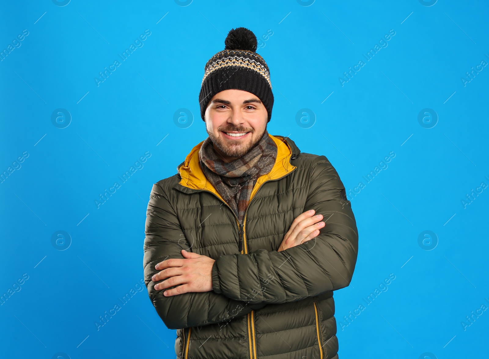 Photo of Happy young man in warm clothes on blue background. Winter vacation