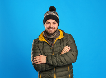 Photo of Happy young man in warm clothes on blue background. Winter vacation