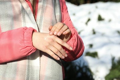 Photo of Woman applying moisturizing cream on hands in winter, closeup