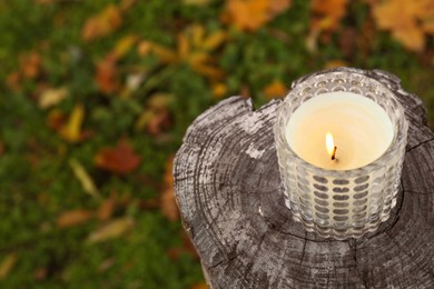 Burning candle on wooden surface outdoors, above view with space for text. Autumn atmosphere