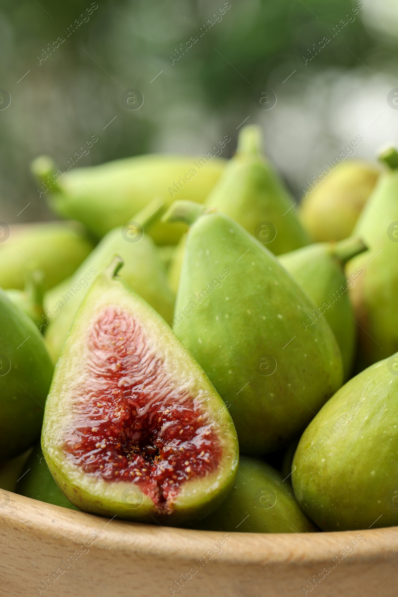 Photo of Cut and whole fresh green figs in wooden bowl against blurred background, closeup