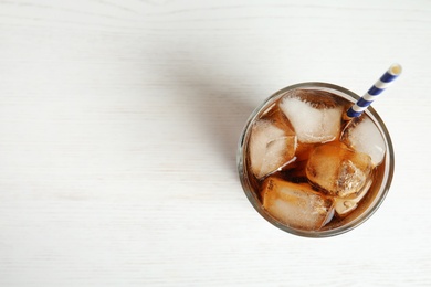 Photo of Glass of refreshing soda drink with ice cubes and straw on white wooden background, top view. Space for text