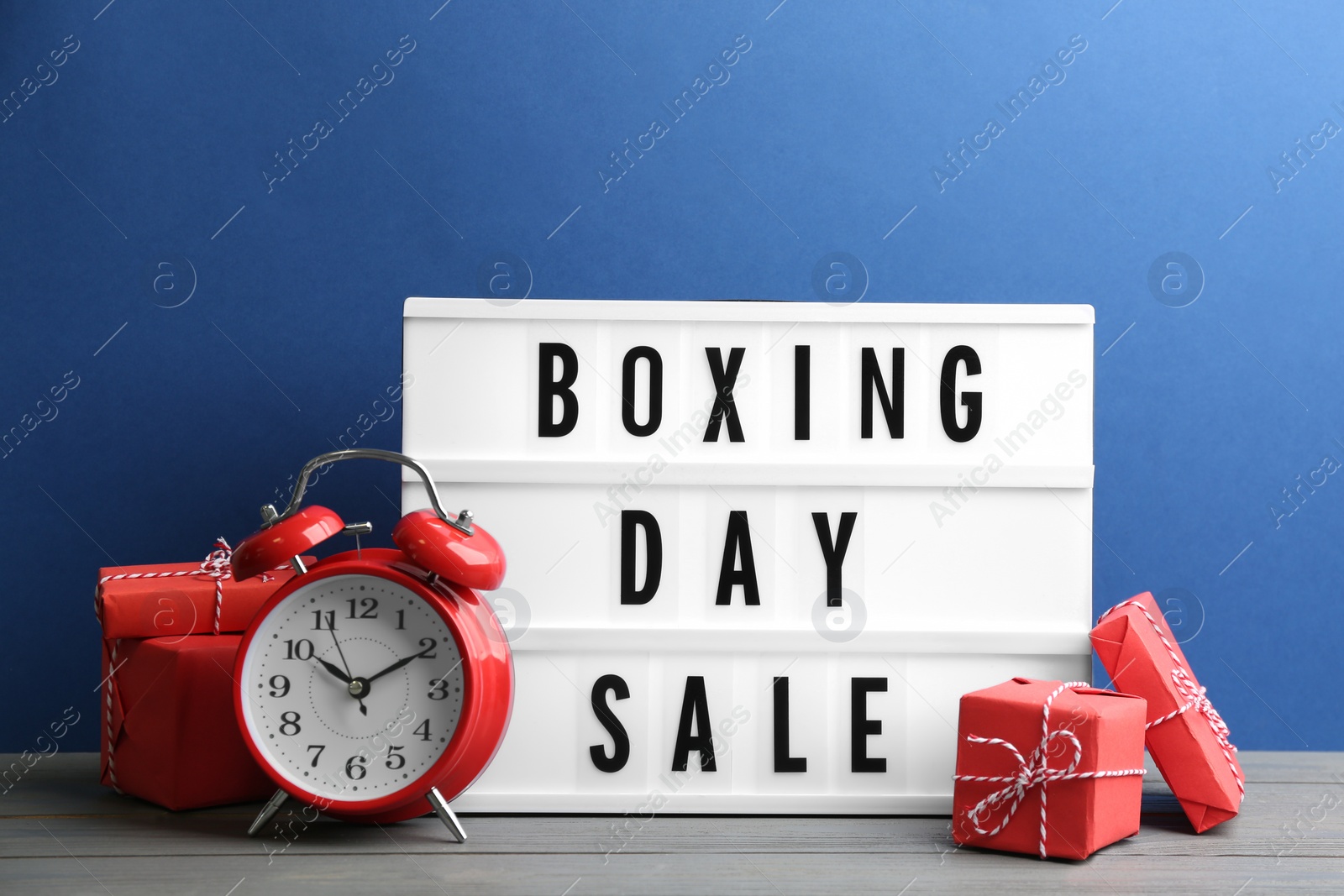 Photo of Composition with Boxing Day Sale sign and Christmas gifts on white table against blue background