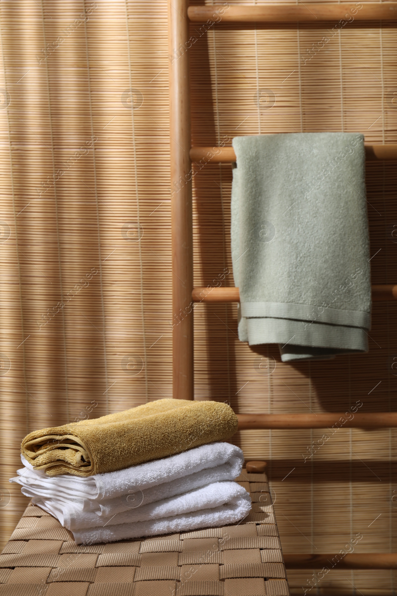 Photo of Stacked soft towels on wicker bench indoors