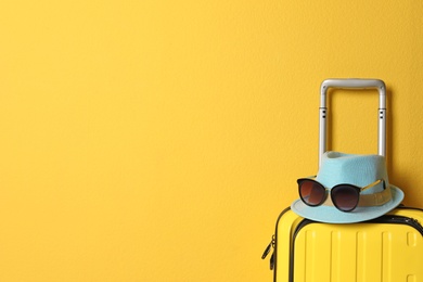 Photo of Bright yellow suitcase with hat and sunglasses on color background