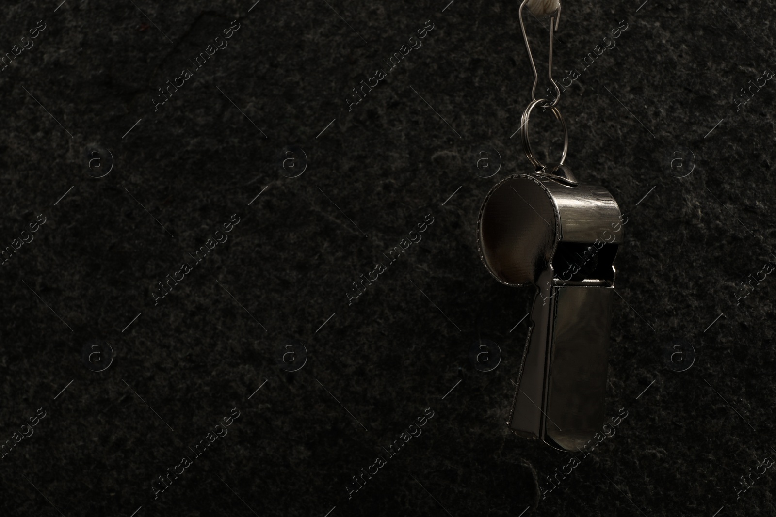 Photo of Referee equipment. Metal whistle on black textured background, closeup and space for text