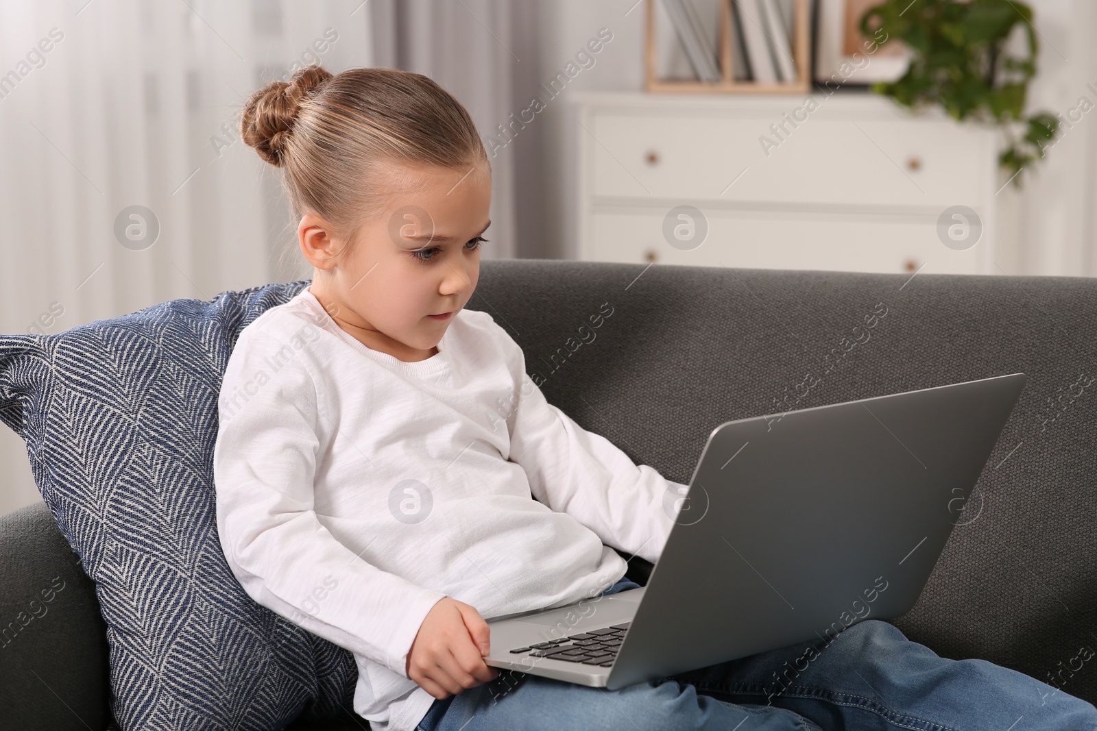 Photo of Little girl using laptop on sofa at home. Internet addiction