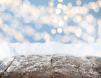 Image of Wooden surface with heap of snow and blurred Christmas lights on background, bokeh effect 