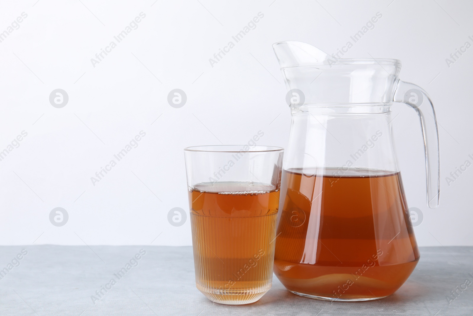 Photo of Homemade fermented kombucha in glass and jug on light grey table. Space for text