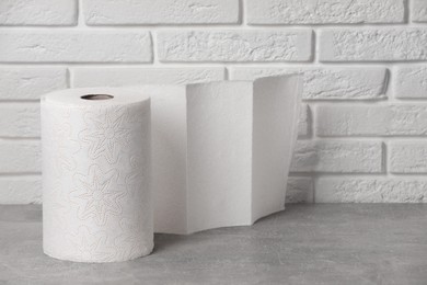 Photo of Roll of white paper towels on grey table near brick wall. Space for text