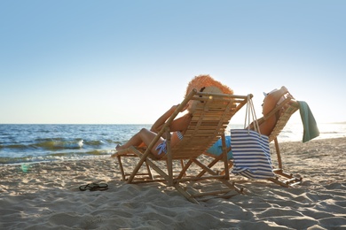 Young couple relaxing in deck chairs on beach near sea