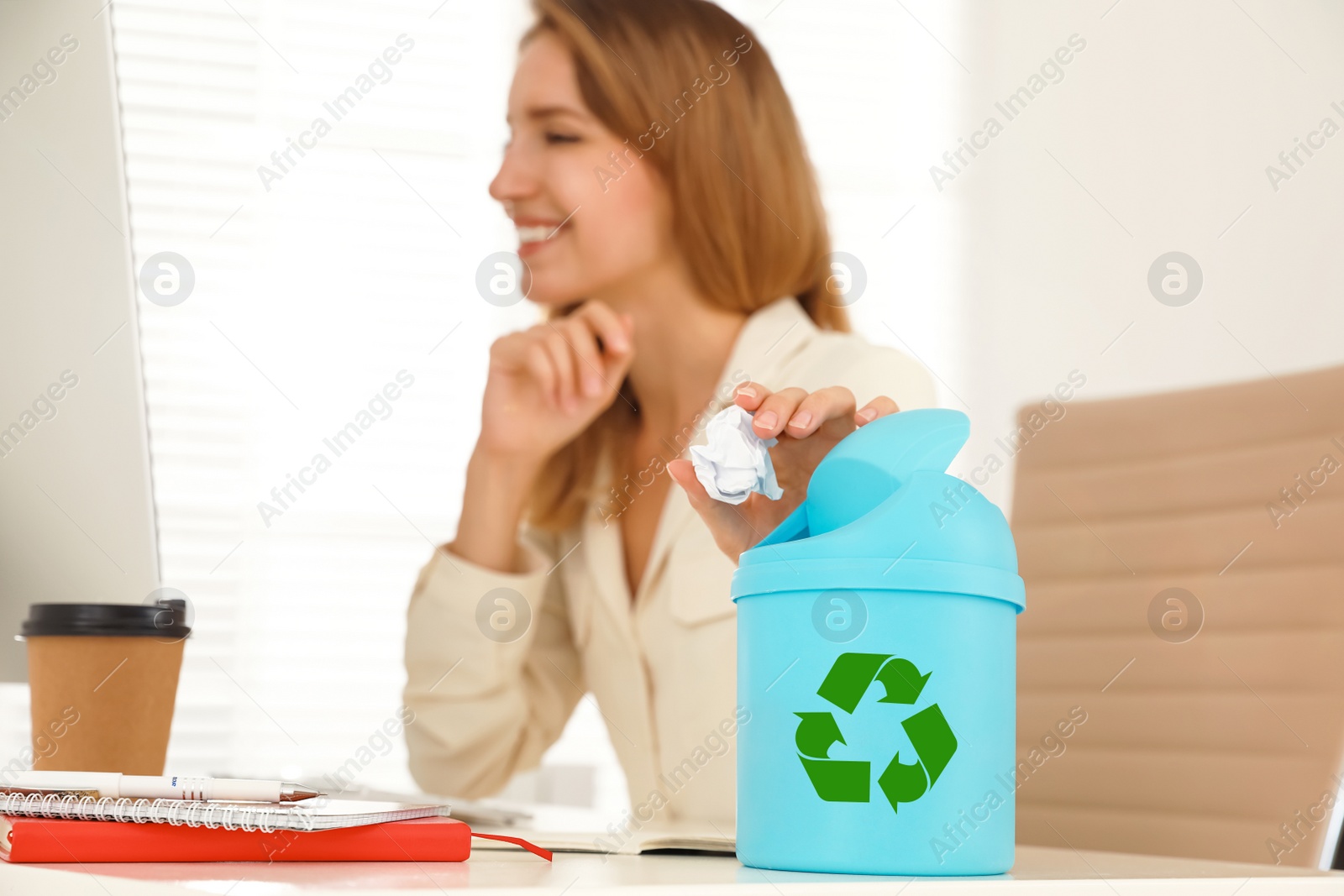 Photo of Young woman throwing paper into mini recycling bin at office