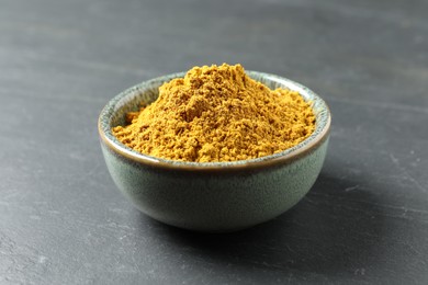 Photo of Dry curry powder in bowl on dark table, closeup