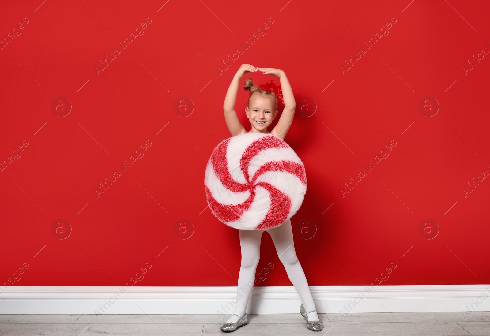 Image of Cute little girl dressed as candy near red wall. Christmas suit