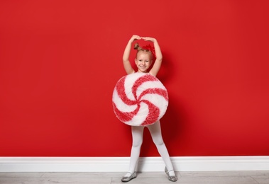 Cute little girl dressed as candy near red wall. Christmas suit