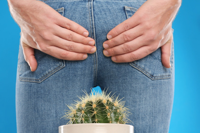 Photo of Man sitting down on cactus against light blue background, closeup. Hemorrhoid concept
