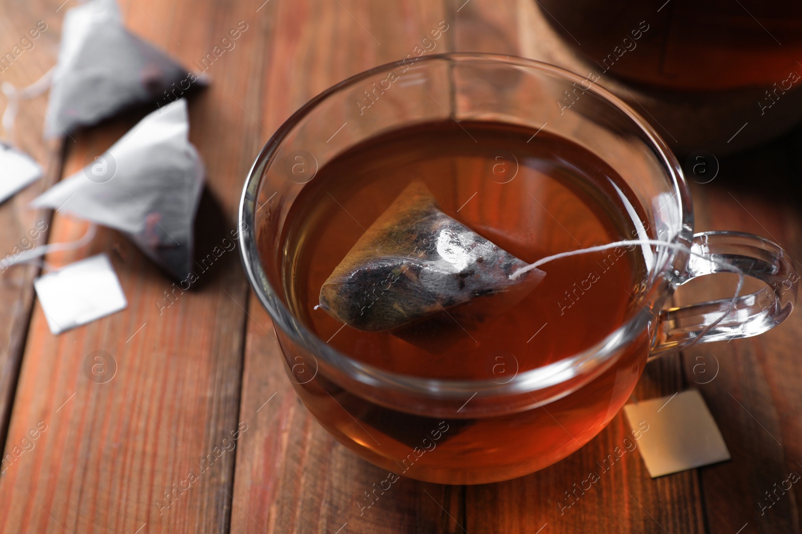 Photo of Tea bag in glass cup on wooden table, closeup