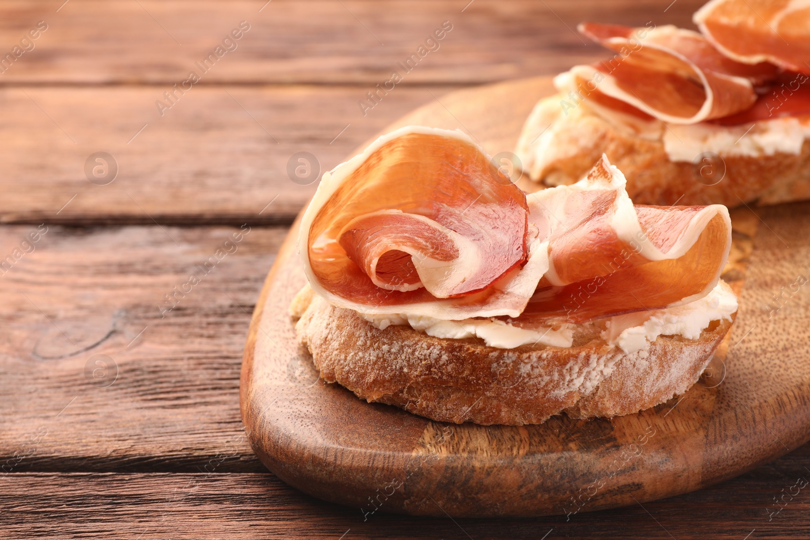 Photo of Board of tasty sandwiches with cured ham and cream cheese on wooden table, closeup. Space for text