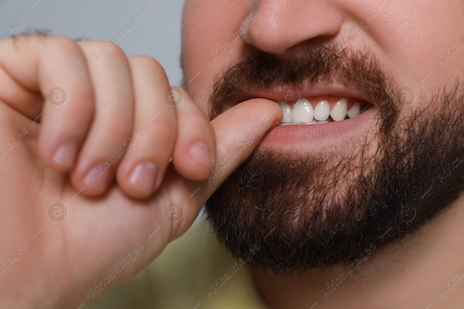 Photo of Man biting his nails on grey background, closeup. Bad habit