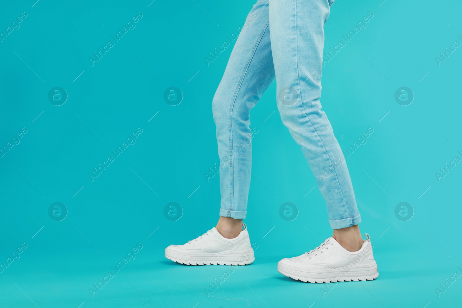 Photo of Woman in stylish sport shoes on light blue background. Space for text