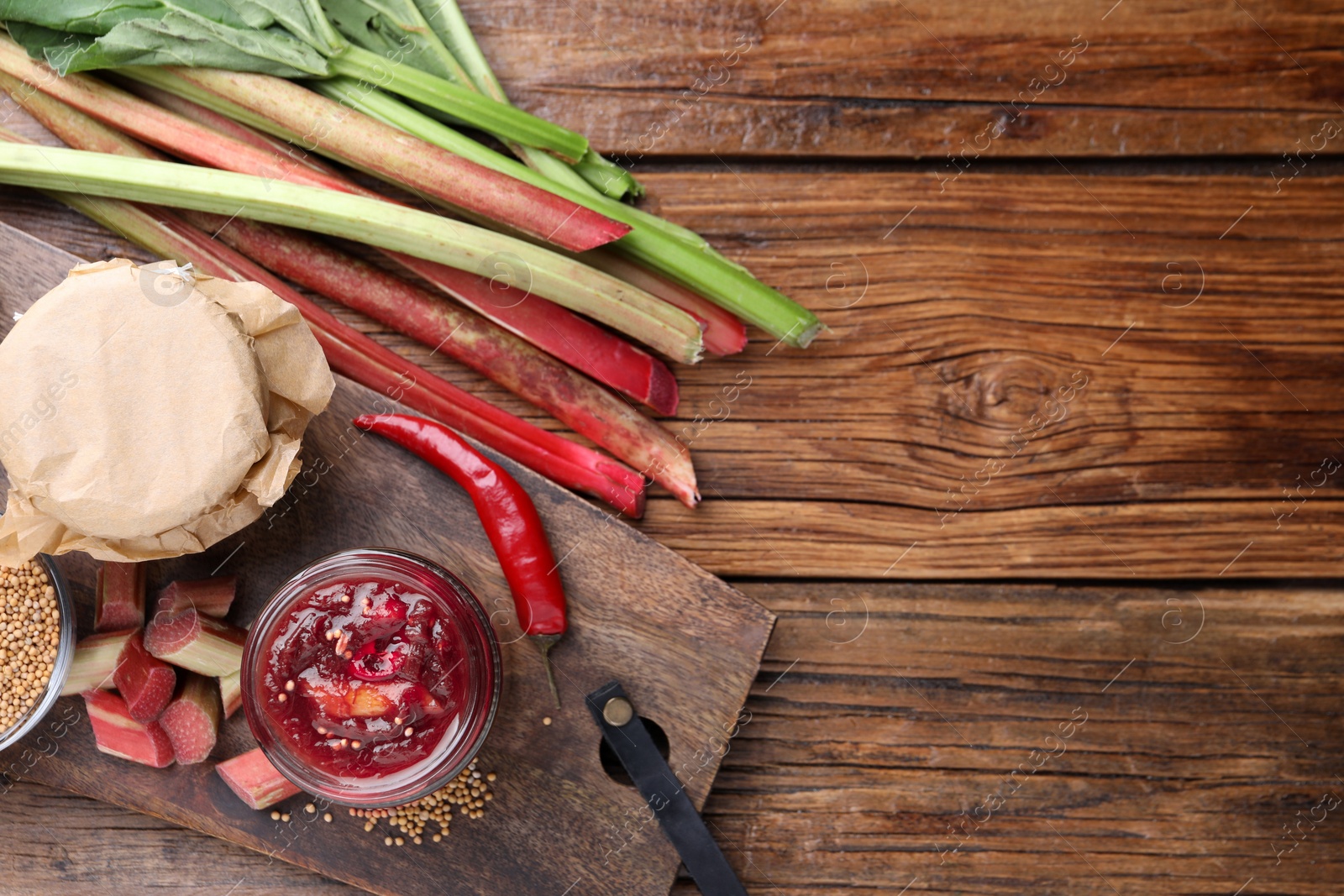 Photo of Tasty rhubarb sauce and ingredients on wooden table, flat lay. Space for text