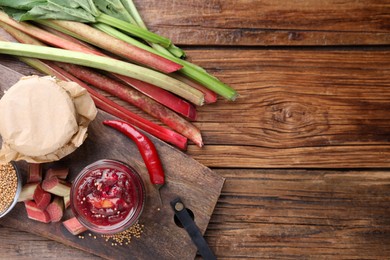 Tasty rhubarb sauce and ingredients on wooden table, flat lay. Space for text