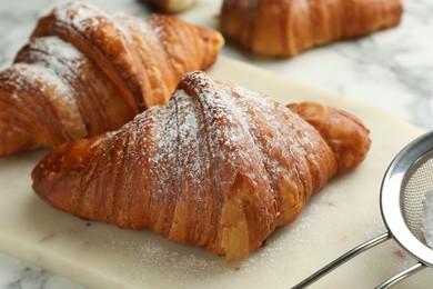 Photo of Tasty croissants with powdered sugar on white marble table, closeup