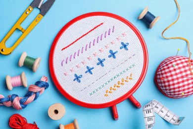 Photo of Flat lay composition with embroidery and different sewing accessories on light blue background