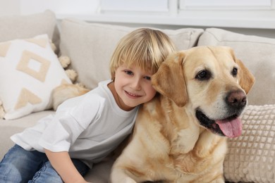 Photo of Cute little child with Golden Retriever on sofa at home. Adorable pet