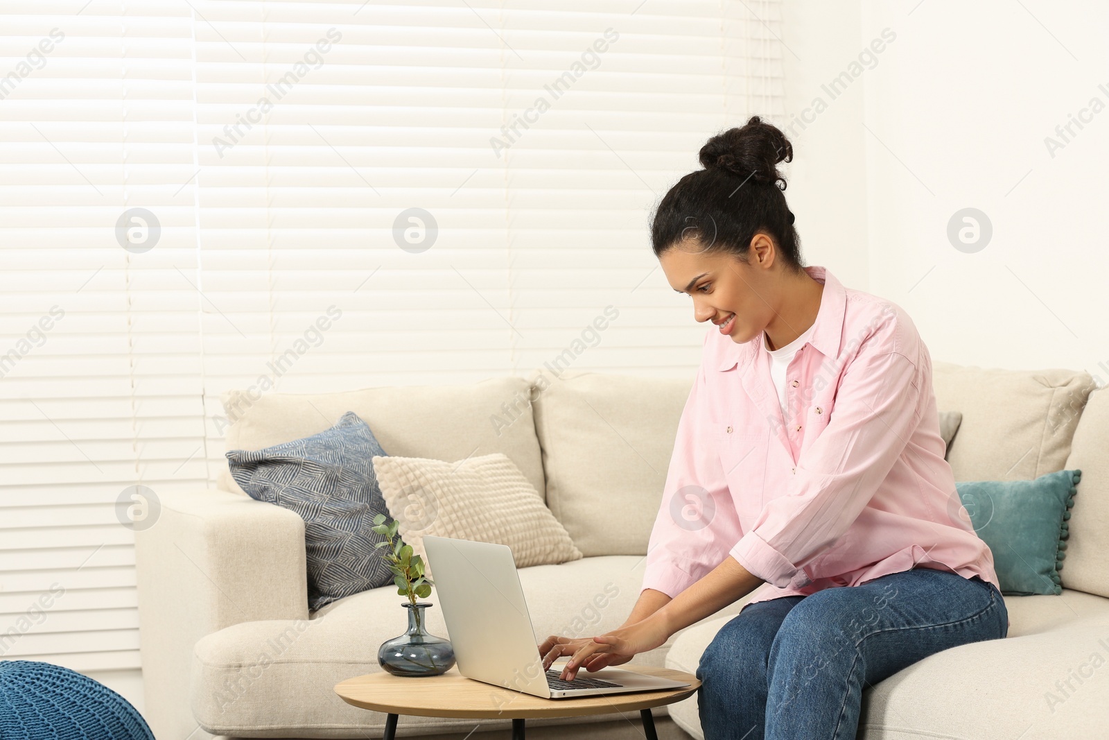 Photo of Smiling African American woman typing on laptop at table in room, space for text