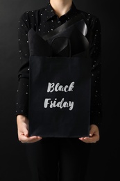 Photo of Woman holding shopping bag with words Black Friday on dark background, closeup