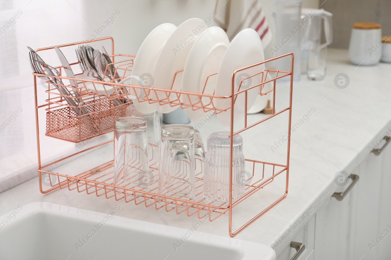 Photo of Drying rack with clean dishes on light marble countertop near sink in kitchen