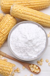 Photo of Bowl with corn starch, ripe cobs and kernels on white wooden table, flat lay