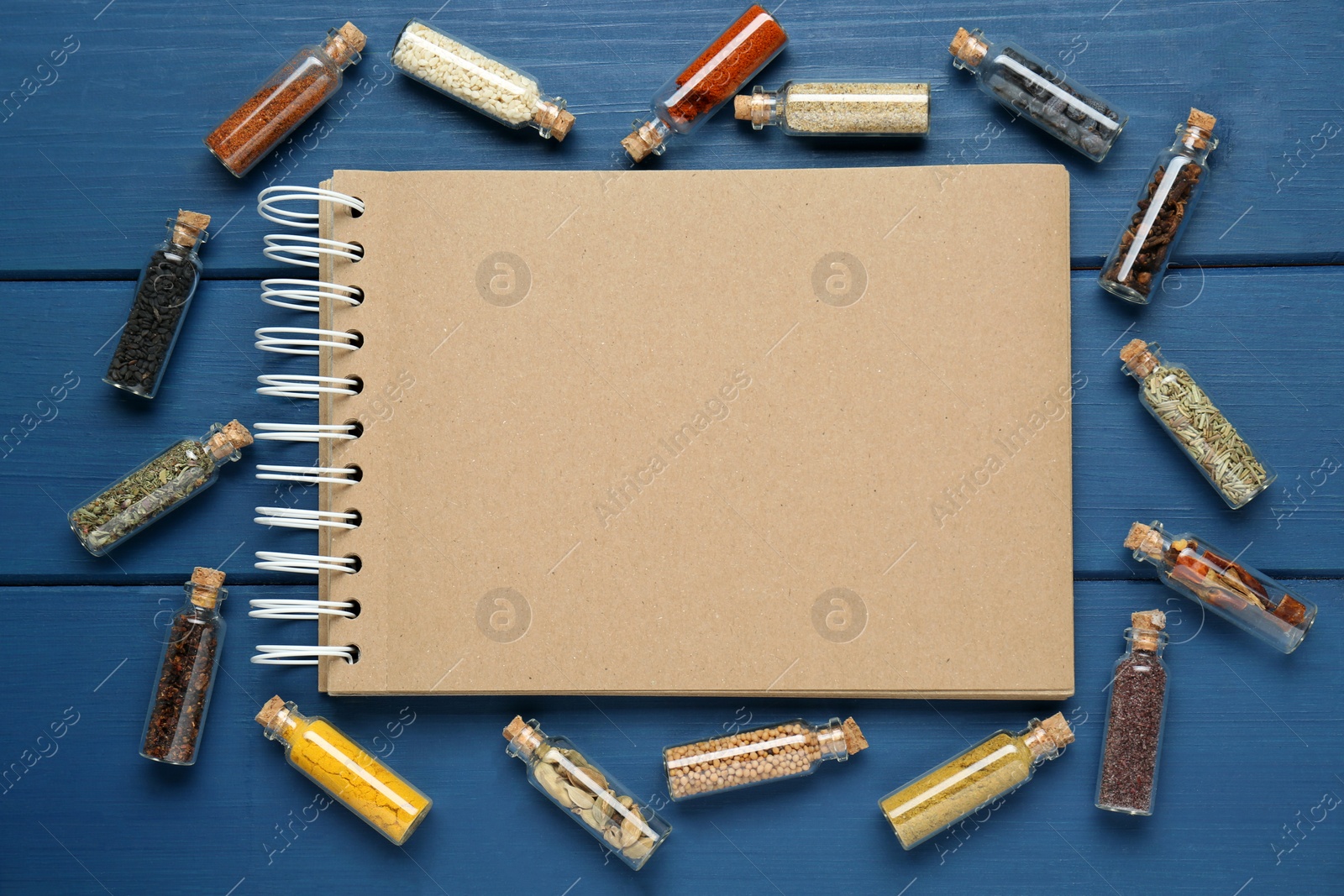 Photo of Blank recipe book and bottles with different spices on blue wooden table, flat lay. Space for text