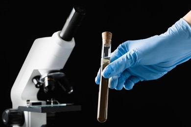 Photo of Scientist holding test tube with liquid against black background, closeup