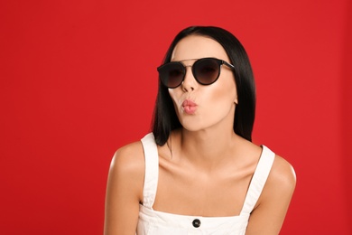 Beautiful woman wearing sunglasses on red background