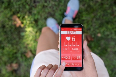 Photo of Young woman using fitness app on smartphone outdoors, top view