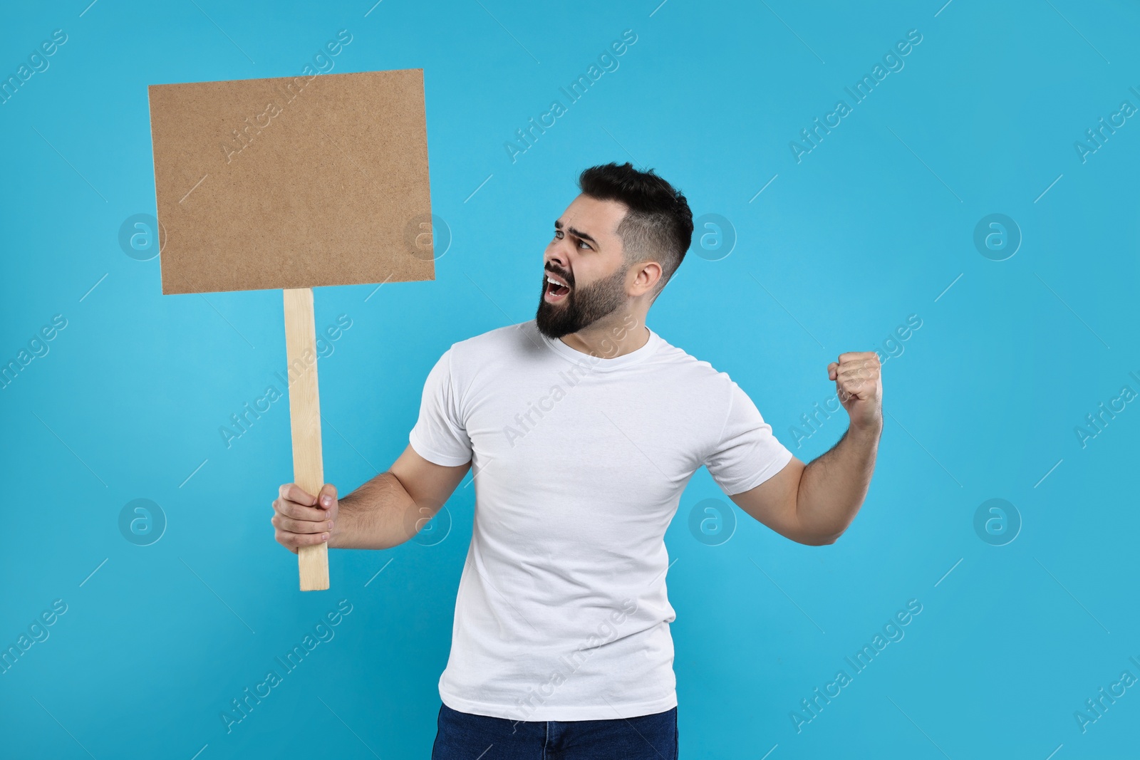 Photo of Angry man holding blank sign on light blue background, space for text