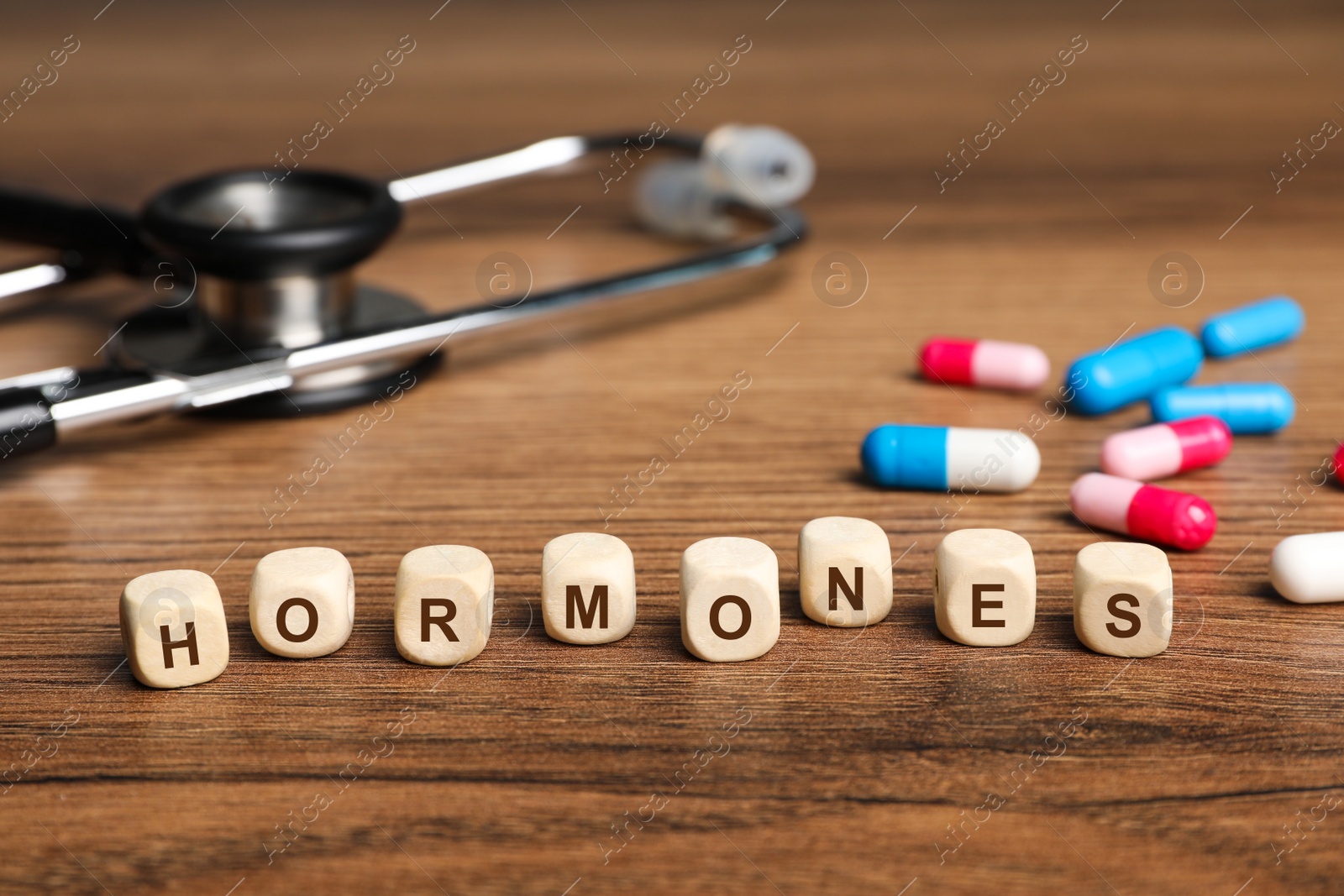 Photo of Word Hormones made of small cubes with letters, stethoscope and pills on wooden table