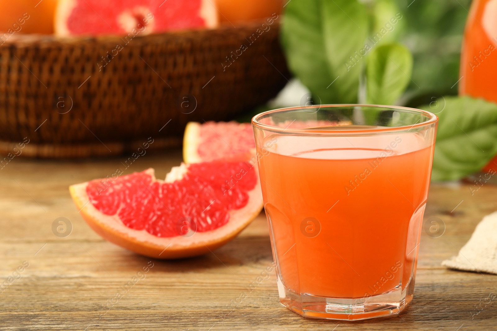 Photo of Glass of delicious grapefruit juice on wooden table against blurred background, space for text