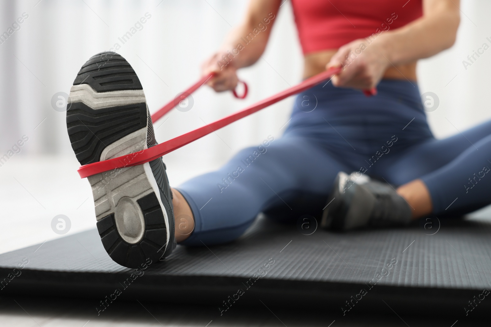 Photo of Woman doing exercise with fitness elastic band on mat indoors, closeup