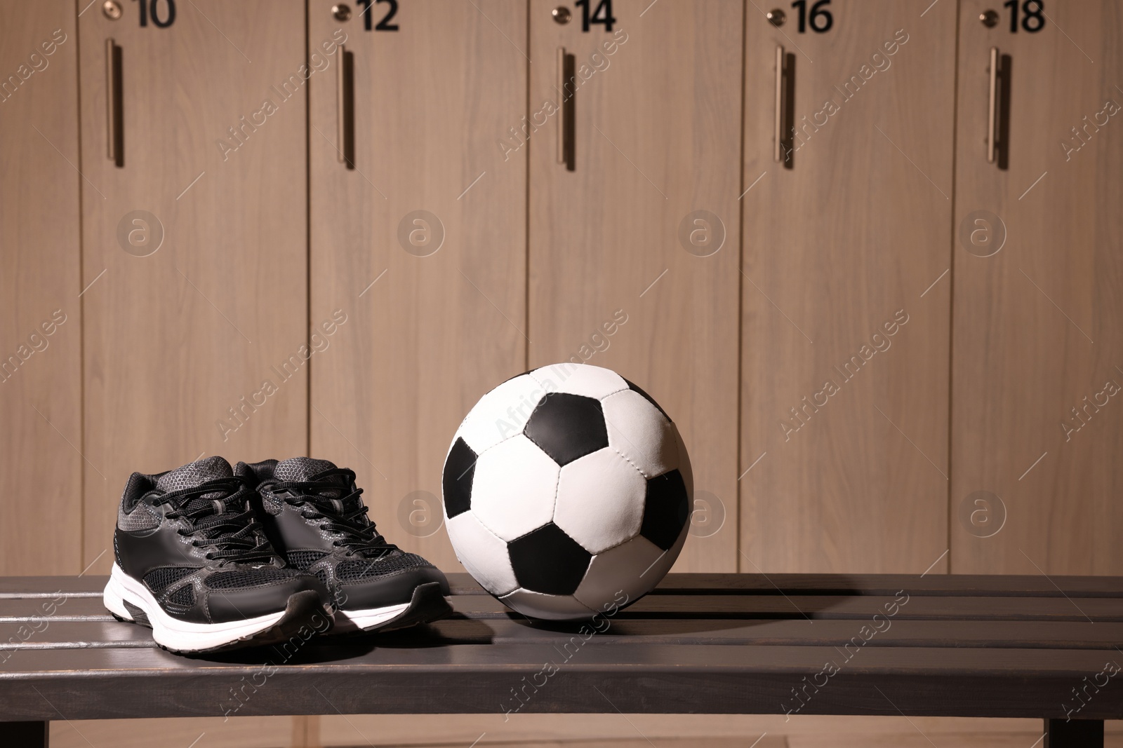 Photo of Soccer ball and sneakers on wooden bench in locker room