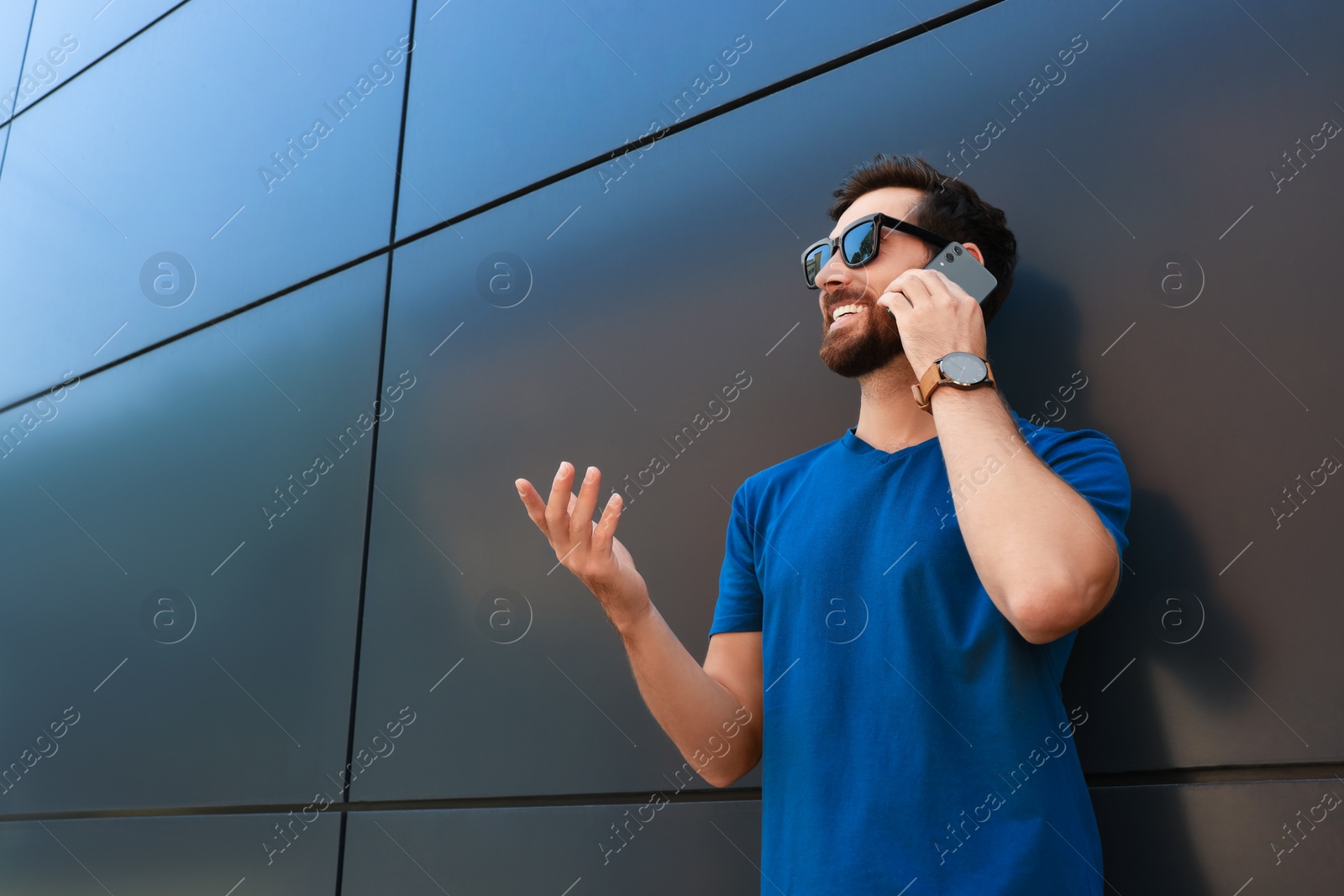 Photo of Happy man talking on phone near grey wall. Space for text