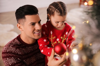 Happy father with his cute daughter decorating Christmas tree together indoors